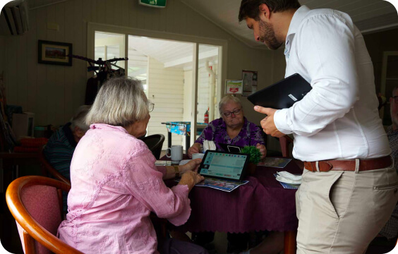 A Conpago team member with older Australians using a tablet at a table